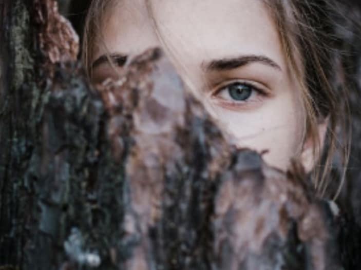 femme à moitié cachée derrière un tronc d'arbre - estime de soi